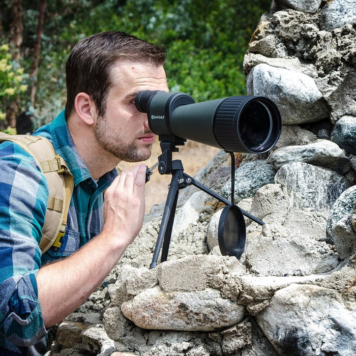 A Man Using the Barska 25-125x88mm WP Benchmark Spotting Scope On Top of Rocks Outdoors
